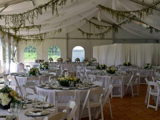 A decorated wedding reception tent at Waldenwoods with round tables, white chairs, floral centerpieces, draped fabric ceiling, and greenery hanging overhead.