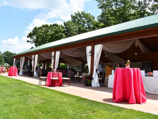 Event at Waldenwoods' Sunshine Cove with draped white curtains, string lights, red-covered tables, and guests seated and mingling on a sunny day.
