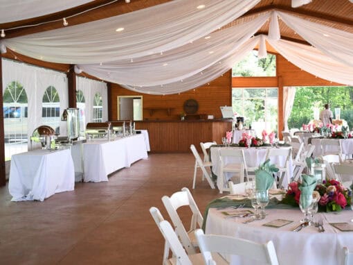 Sunshine Cove decorated with draped white fabric on the ceiling, set tables with floral centerpieces, and buffet tables along the wall.